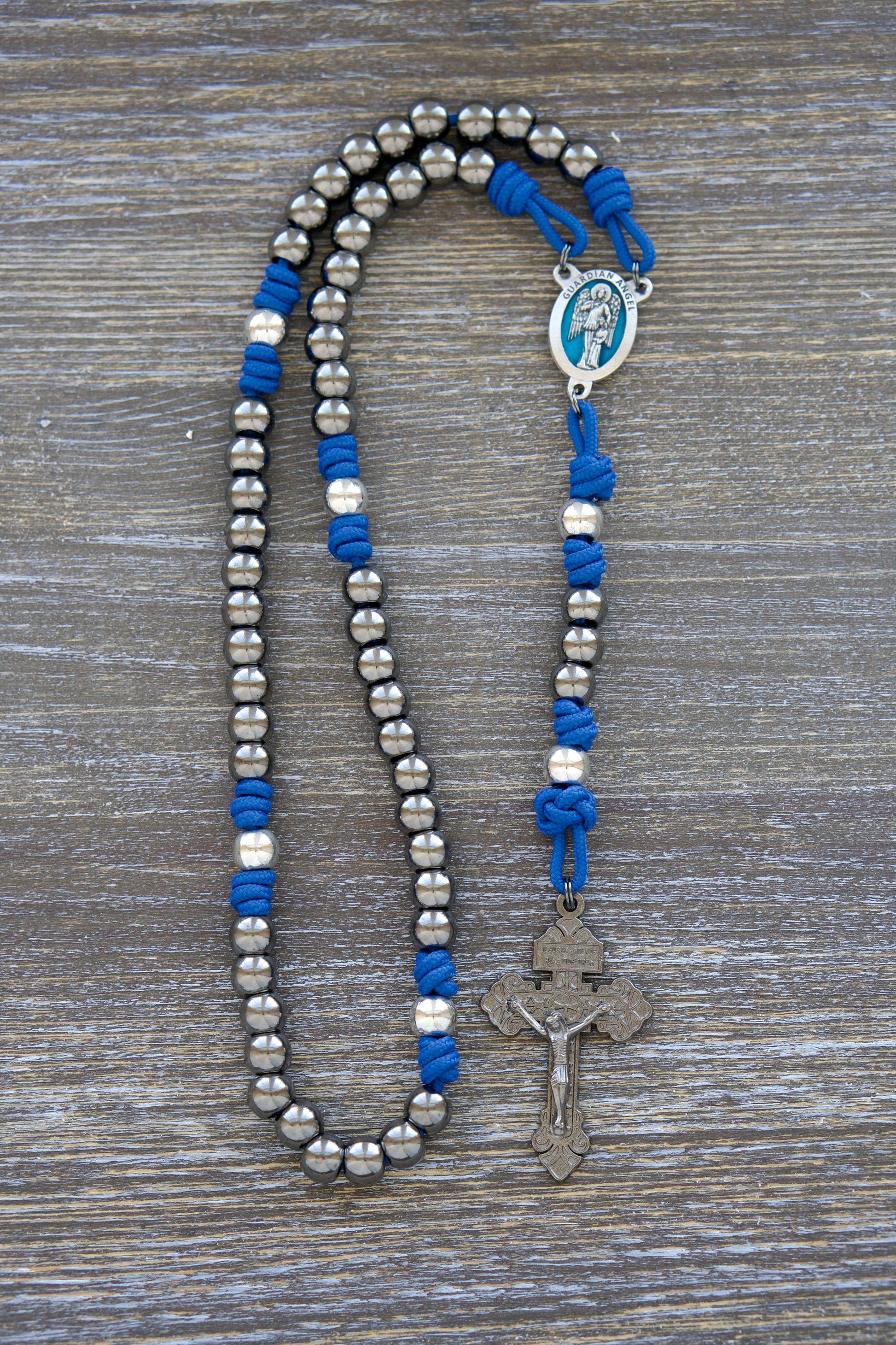 Premium metal paracord rosary featuring a stunning blue enamel Guardian Angel centerpiece. Durable royal blue paracord, gunmetal Hail Mary beads, and silver Our Father beads create an elegant devotional tool for enhancing prayer to your holy Guardian Angel.