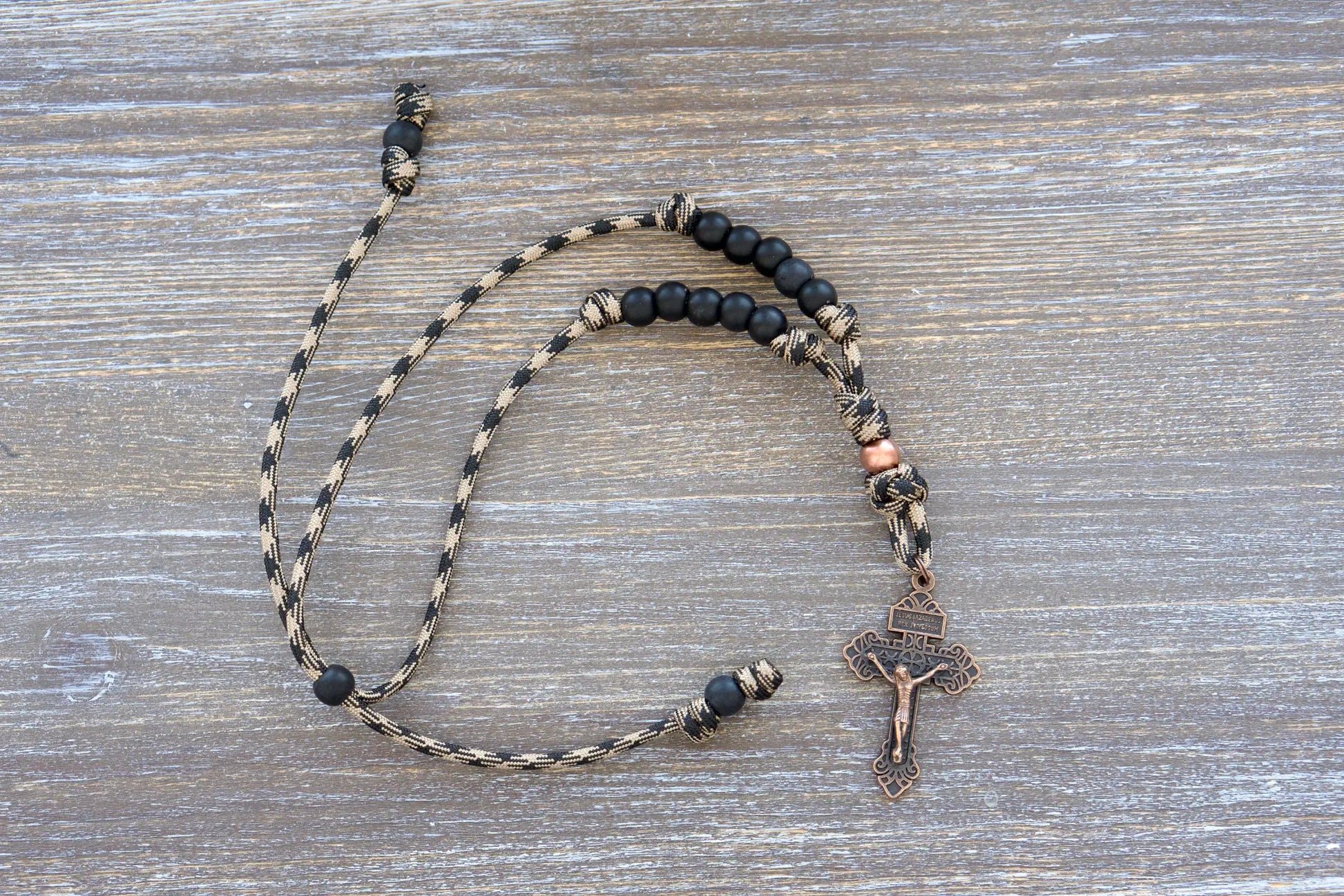 Heavy Duty Hail Mary rearview mirror rosary hangs securely, showcasing 10mm matte black and antique copper beads on rugged 550 paracord with a copper crucifix.