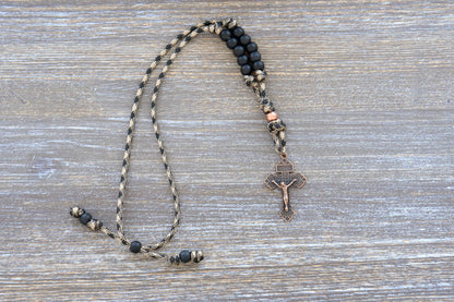 Heavy Duty Hail Mary mirror rosary with camo paracord, matte black and copper beads, antique copper crucifix, securely hung from a car rearview mirror.