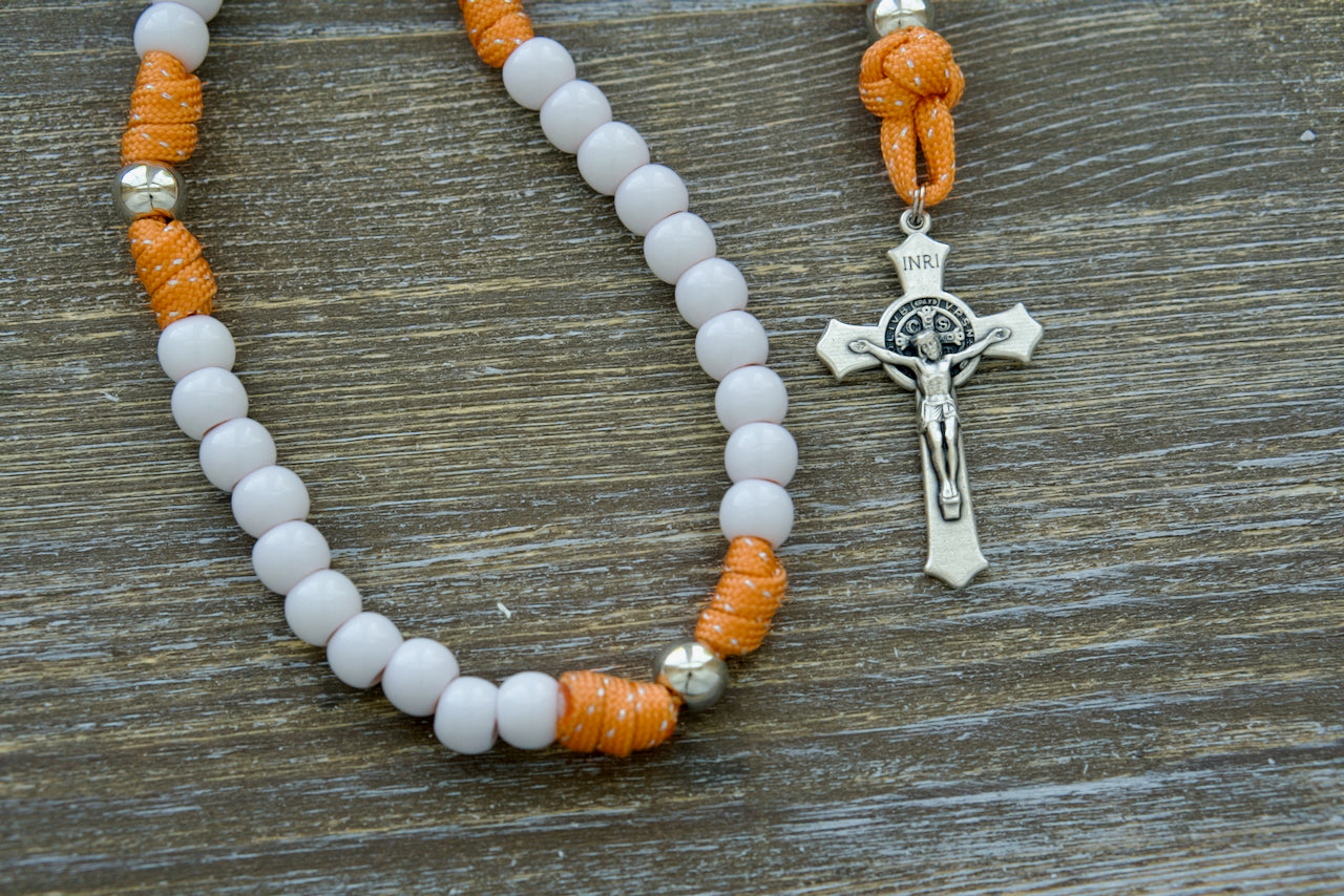 Holy Childhood - Kid's Paracord Rosary: Experience the power of faith and durability with this striking orange-and-silver paracord rosary, featuring white Hail Mary beads, silver Our Father beads, a 2-inch St. Benedict crucifix, and a 0.75-inch Miraculous Medal.