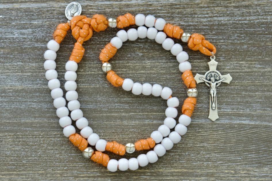 Holy Childhood - Kid's Paracord Rosary with orange and silver design, featuring white Hail Mary beads, silver Our Father beads, a 2-inch St. Benedict crucifix, and a 0.75-inch Miraculous Medal. Made with premium, unbreakable paracord for durability in your spiritual journey.