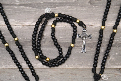The Holy Servant Paracord Rosary features black beads, gold accents, and a large St. Benedict crucifix.