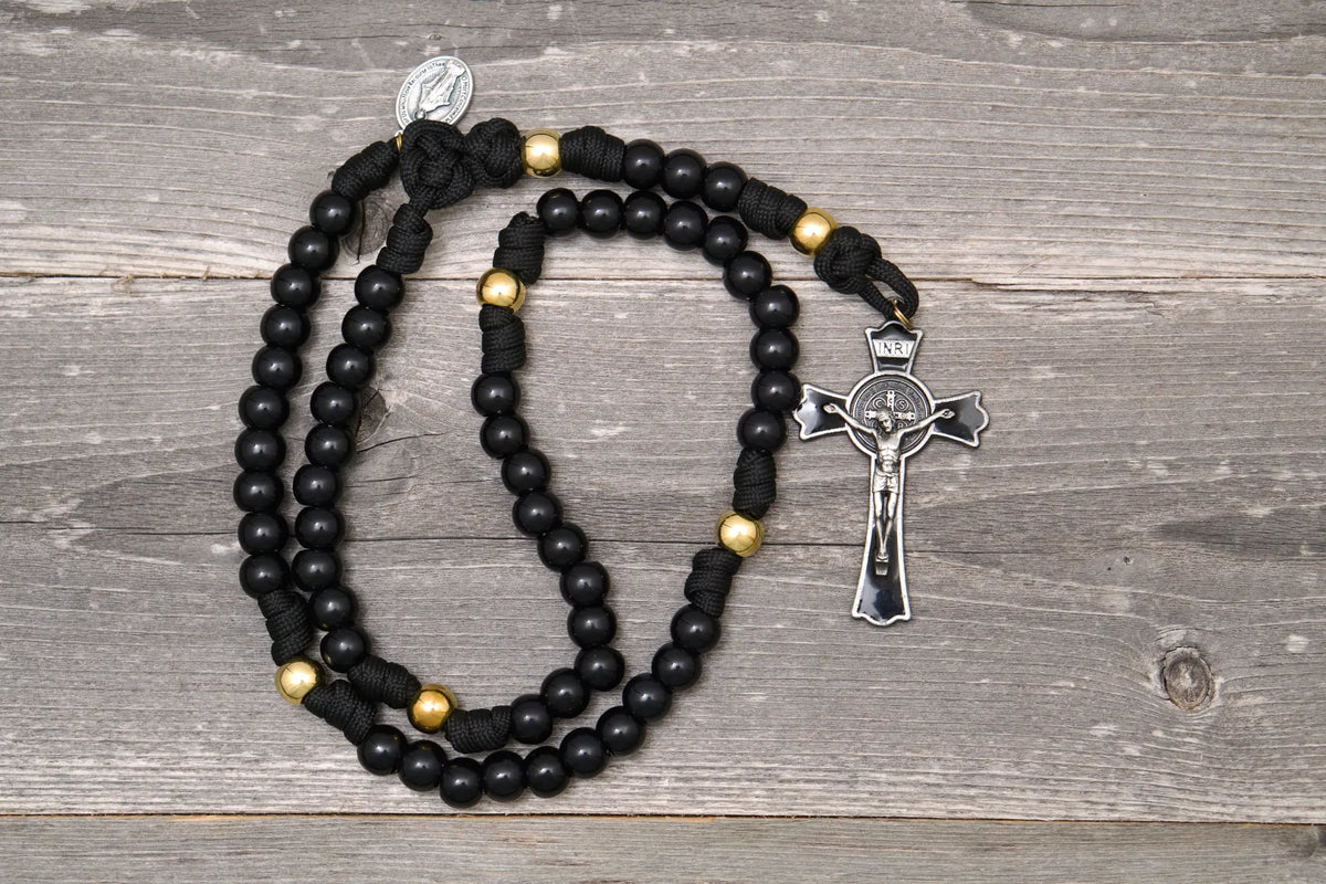 The Holy Servant Rosary featuring black paracord, shiny gold and black beads, and a large St. Benedict crucifix.