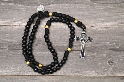 The Holy Servant Rosary featuring black paracord, shiny gold and black beads, and a large St. Benedict crucifix.