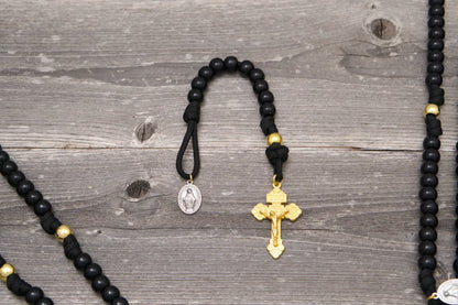 The Holy Servant Paracord Rosary features black beads, gold accents, a Miraculous Medal, and a gold Pardon crucifix.