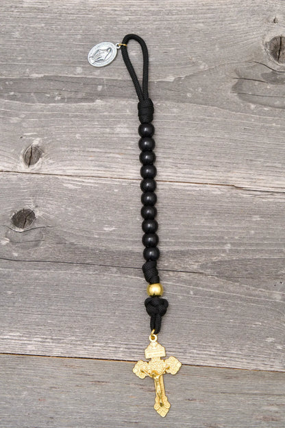 The Holy Servant Rosary features black paracord, glossy beads, a Miraculous Medal, and a gold St. Benedict crucifix.