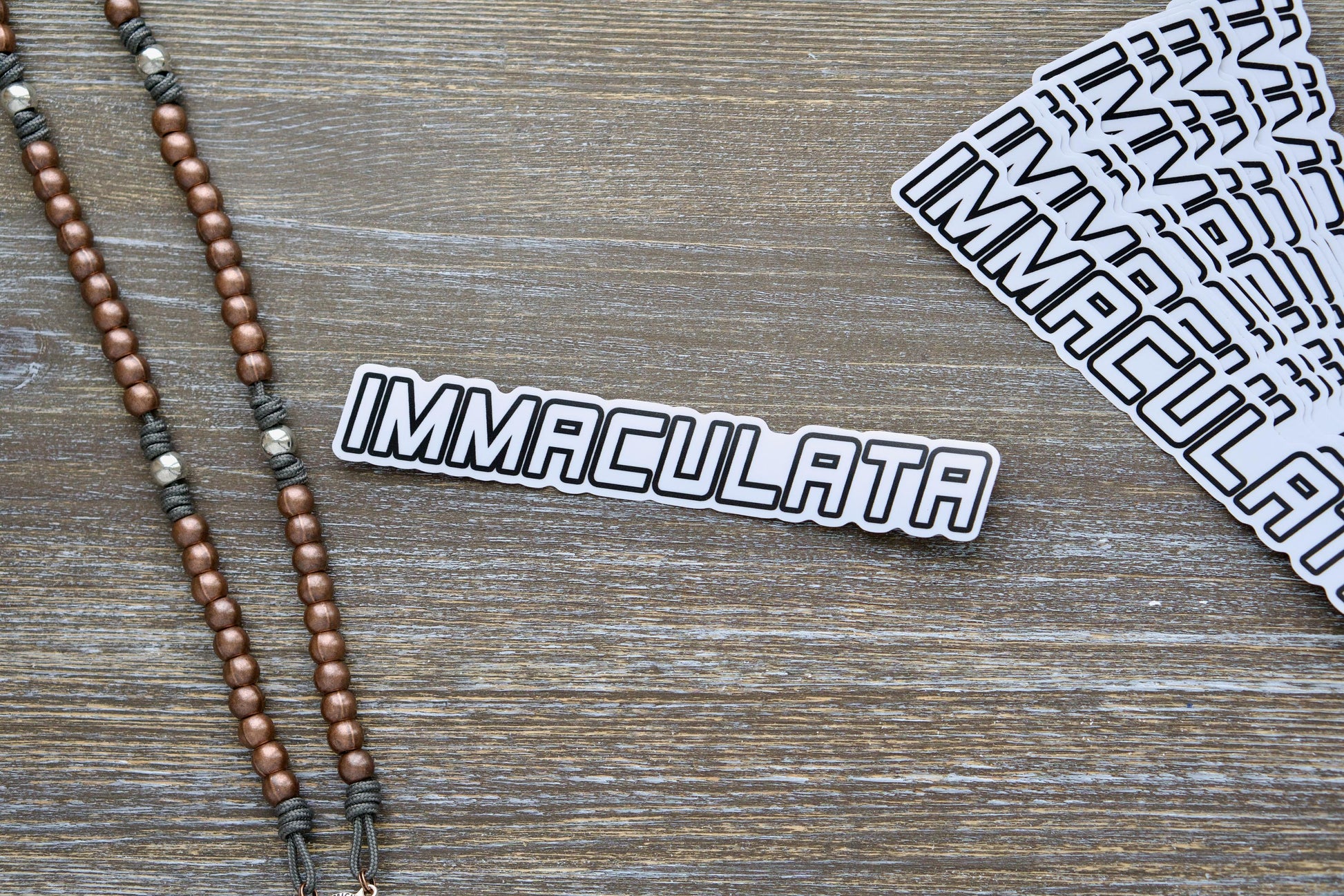 Immaculata Vinyl Sticker featuring a bold graphic representing St. Maximilian Kolbe's Militia of Immaculata. 7.17" wide x 1.14" tall, removable white semi-gloss vinyl with matte laminate for durability and UV resistance, suitable for indoor/outdoor use on various surfaces.  Show your support for the fight against heresy and modernism while spreading the Catholic faith.