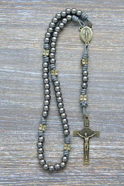 A handcrafted paracord rosary featuring gunmetal Hail Mary beads, an olive Miraculous Medal centerpiece, and a matching St. Benedict crucifix, iron gray rope.