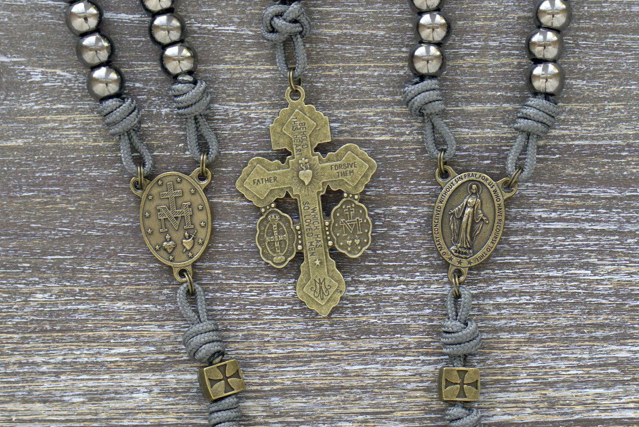 A rugged, handcrafted Iron Crusader paracord rosary featuring olive green crusader Our Father beads, gunmetal Hail Mary beads, a Miraculous Medal centerpiece, and a matching "Triple Threat" pardon crucifix.