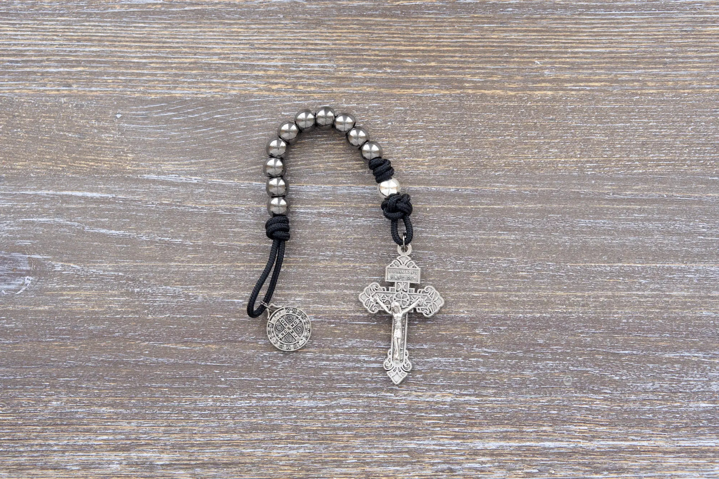 Iron Resolve pocket paracord rosary with black cord, gunmetal beads, crucifix, and Benedict medal.