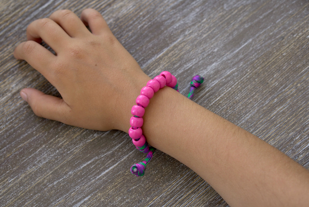 Kid's Judith's Sword Rosary Bracelet by Sanctus Servo, featuring purple and green paracord rope with pink Hail Mary beads, petite Our Father bead, and a Miraculous Medal.