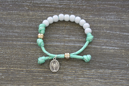 Children's Mint Green Kid's Rosary Bracelet from Sanctus Servo, featuring mint green rope with rainbow ribbon intertwined, white beads for Hail Mary prayers, and a rose gold Our Father bead.