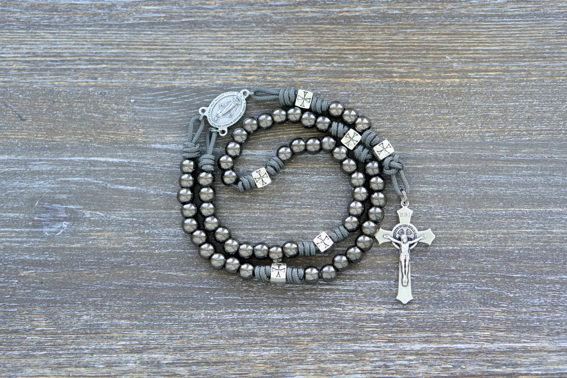 Last Stand Rosary: Gunmetal Hail Mary beads, silver crusader Our Father beads, Miraculous Medal centerpiece, and 2-inch St. Benedict crucifix on durable gray paracord.