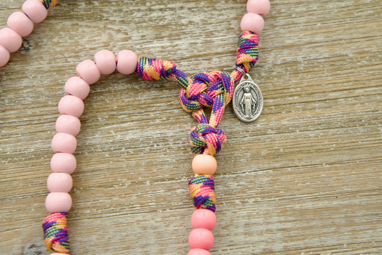 Beautiful pink camo rosary designed for little girls, featuring durable paracord, light pink Hail Mary beads, peachy orange Our Father bead, and a smaller Miraculous Medal. Perfect for introducing Catholic prayer to young children while being strong and unbreakable.