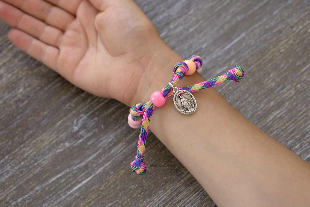 Little Lady's Miracle - Kid's Rosary Bracelet: A beautiful pink/green/orange paracord rosary bracelet with 10mm acrylic beads, orange Our Father beads, and a tiny Miraculous Medal charm for young Catholics to nurture their spiritual journey.