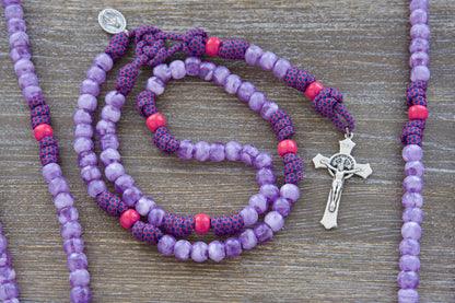 Vibrant paracord rosary designed for children, featuring milky purple and pink 10mm acrylic beads, a mini Miraculous Medal, and a 2-inch St. Benedict crucifix.