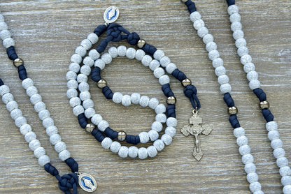 Marian Stronghold - 5 Decade Paracord Rosary: Handmade, durable Catholic gift featuring navy blue paracord, gunmetal Our Father beads, and cracked ivory Hail Mary beads; complete with a 2-inch gunmetal Pardon Crucifix and blue enamel Miraculous Medal for unparalleled devotion.