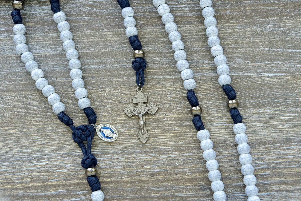 Marian Stronghold - 5 Decade Paracord Rosary with navy blue rope, gunmetal Our Father beads, cracked ivory Hail Mary beads, and matching 2-inch gunmetal Pardon Crucifix, perfect for young Catholics seeking spiritual strength and devotion.