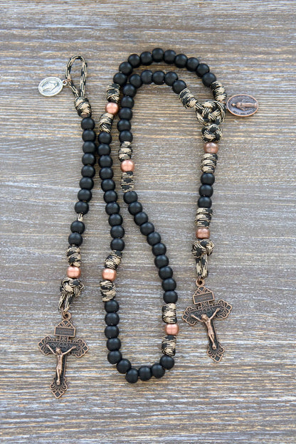 This kid's Mini Duty Hail Mary rosary features rugged camo black and brown 550 paracord, small 10mm matte black beads, copper accents, and a Pardon crucifix.