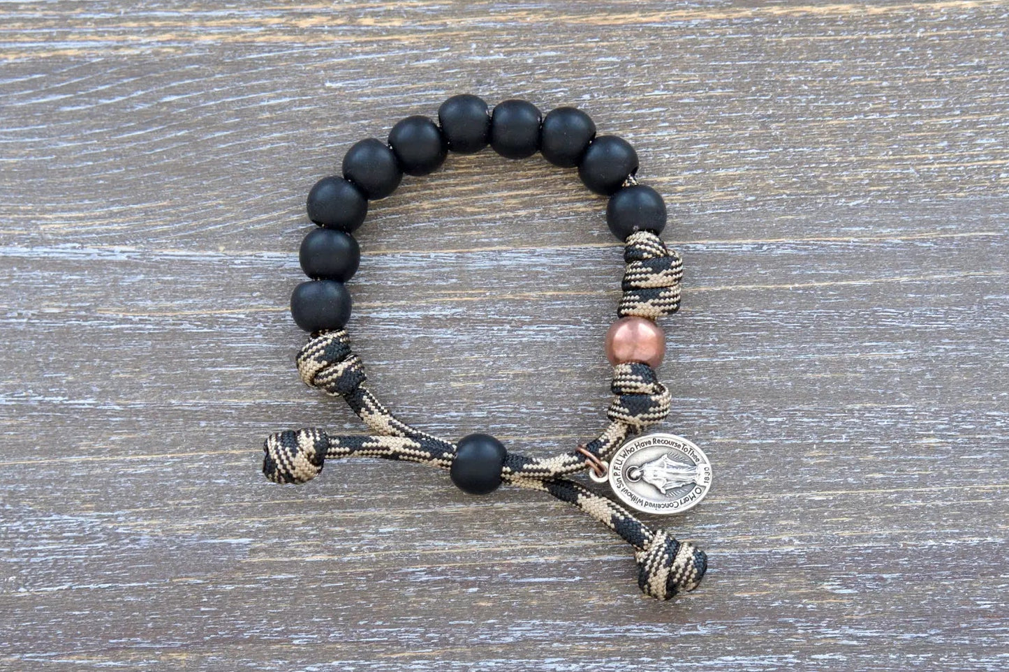 Mini Duty Hail Mary kids bracelet features rugged 10mm matte black beads, an antique copper Our Father bead, and a small Miraculous Medal on durable paracord.