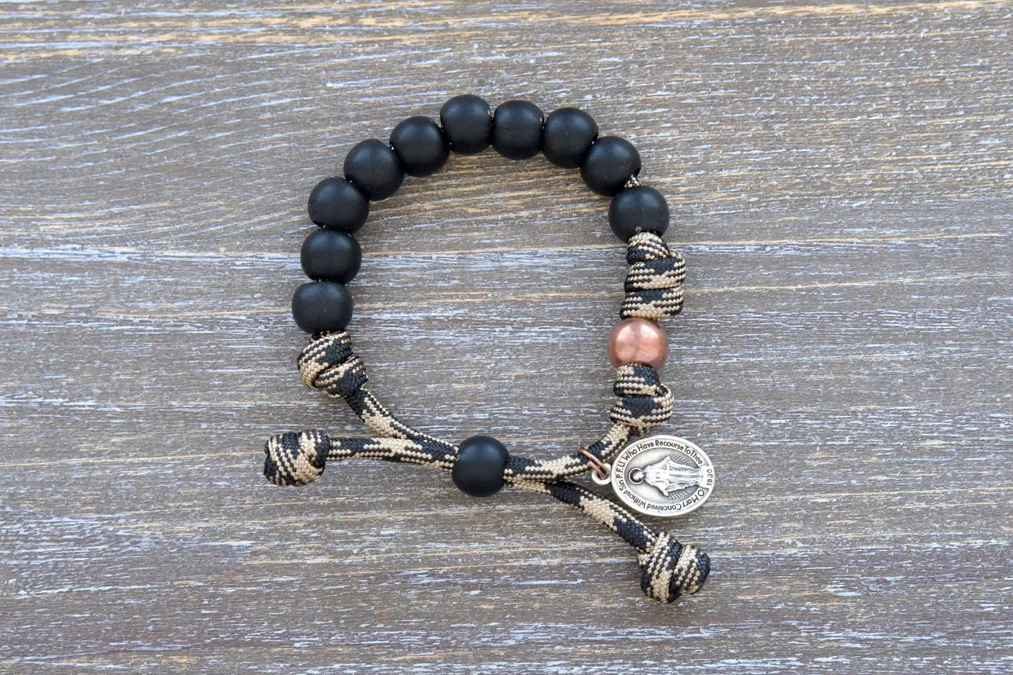 Mini Duty Hail Mary kids bracelet features rugged 10mm matte black beads, an antique copper Our Father bead, and a small Miraculous Medal on durable paracord.