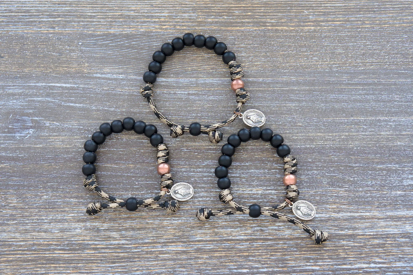 This mini duty rosary bracelet features 10mm matte black Hail Mary beads, an antique copper Our Father bead, and a sacred Miraculous Medal on rugged paracord.