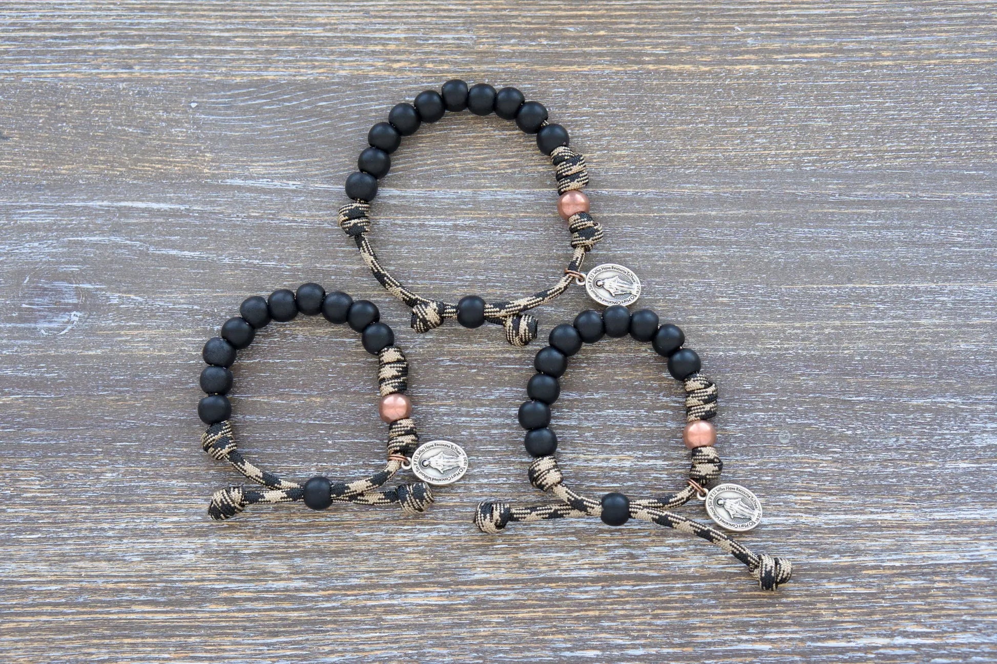 This mini duty rosary bracelet features 10mm matte black Hail Mary beads, an antique copper Our Father bead, and a sacred Miraculous Medal on rugged paracord.