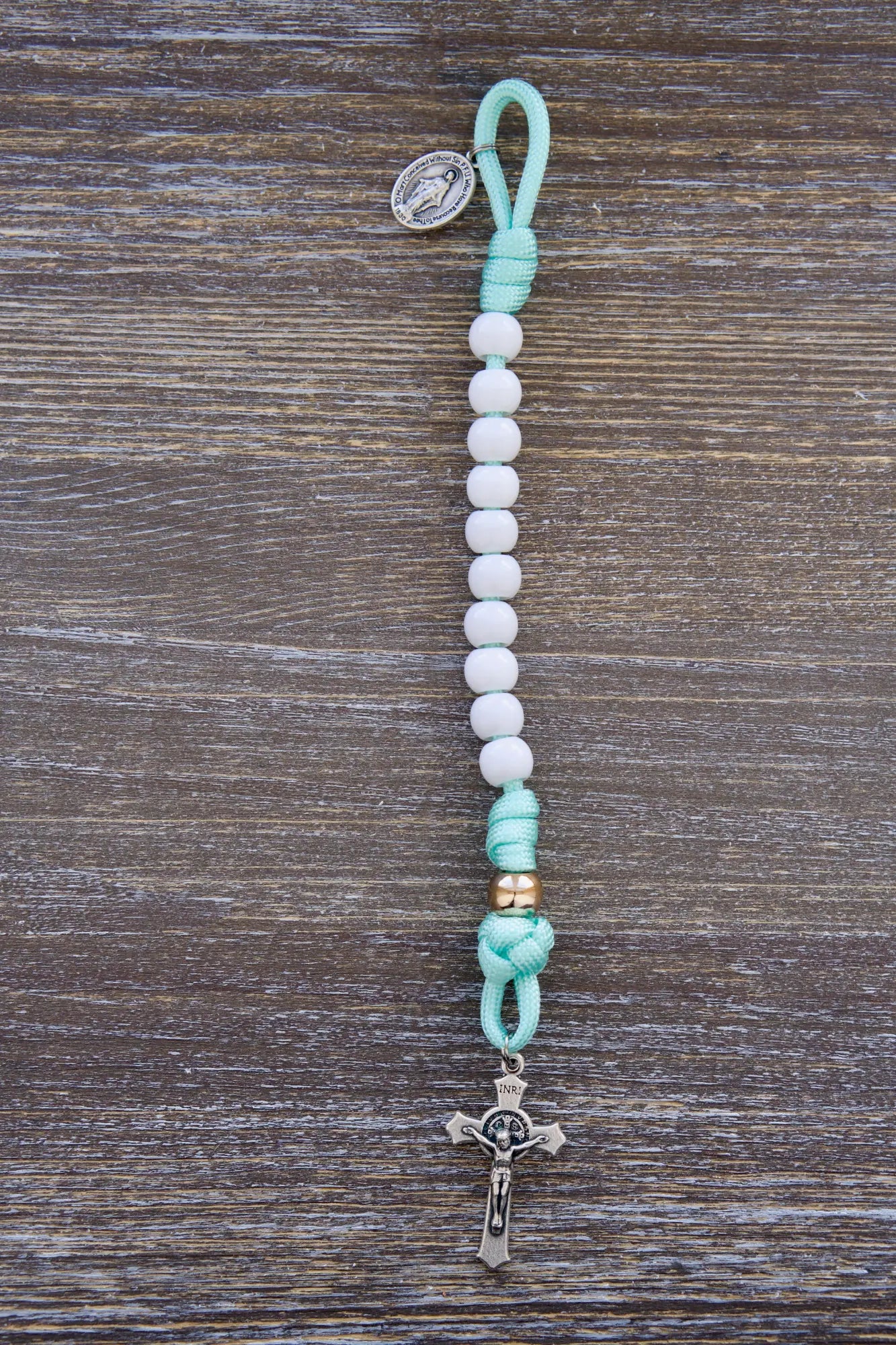 Mint green paracord rosary with white Hail Mary and rose gold Our Father beads, featuring small Miraculous Medal and St. Benedict crucifixes.