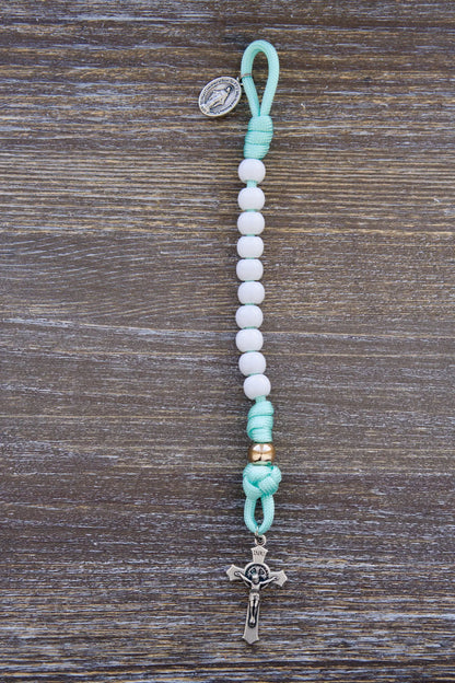 Mint green paracord rosary with white Hail Mary and rose gold Our Father beads, featuring small Miraculous Medal and St. Benedict crucifixes.