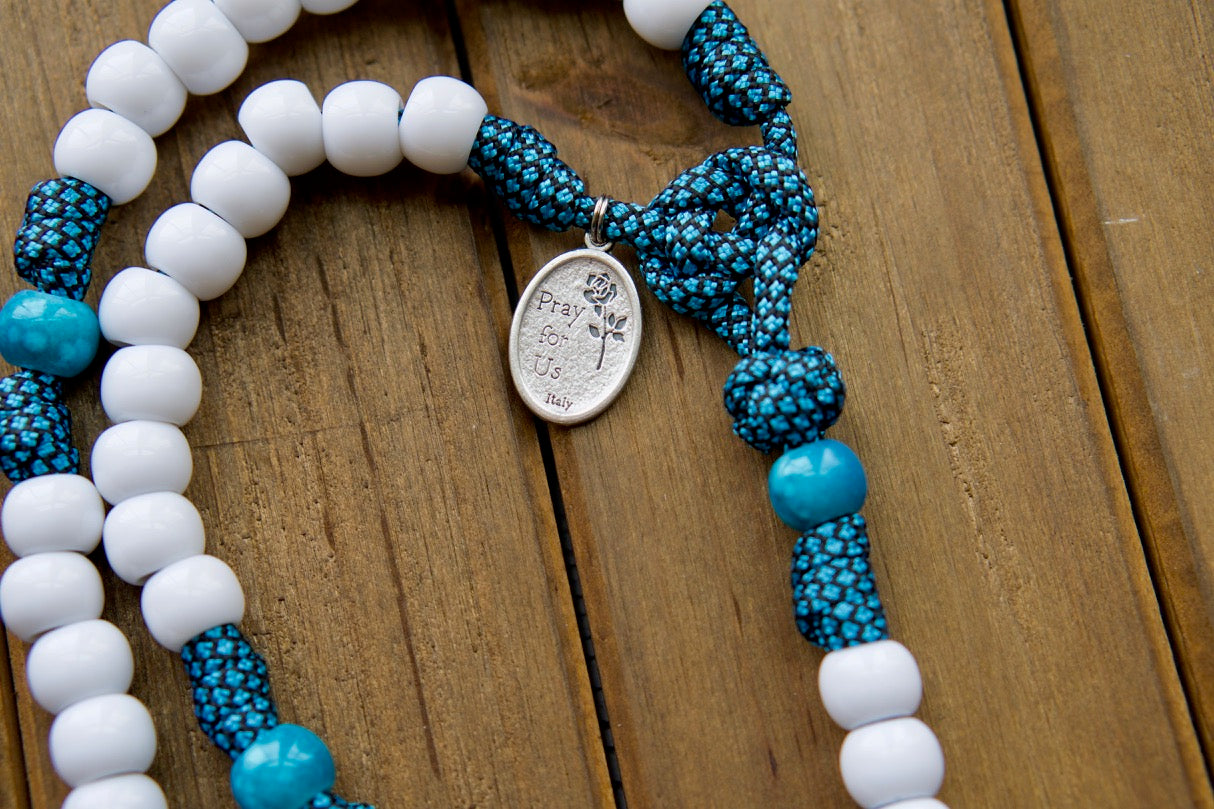 Our Lady of Perpetual Help - Turquoise - 5 Decade Paracord Rosary: A durable and unbreakable paracord rosary designed to withstand life's battles while remaining a powerful spiritual weapon. Featuring an exclusive Our Lady of Perpetual Help design, white Hail Mary beads, matching turquoise Our Father beads, and a large 3" white enamel St. Benedict Crucifix. 