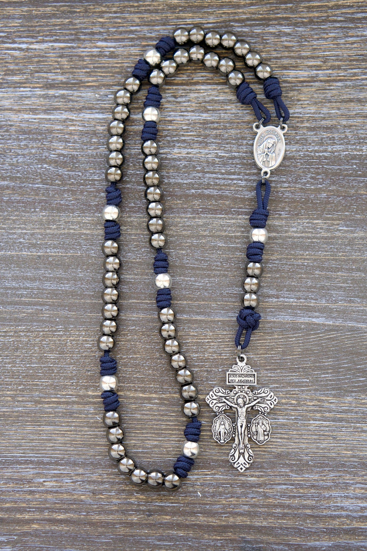 A handcrafted navy blue Servite Rosary chaplet featuring gunmetal Hail Mary beads, radiant silver Our Father beads, and a centerpiece medal depicting Our Lady of Sorrows (Mater Dolorosa) on one side and Ecce Homo on the other.