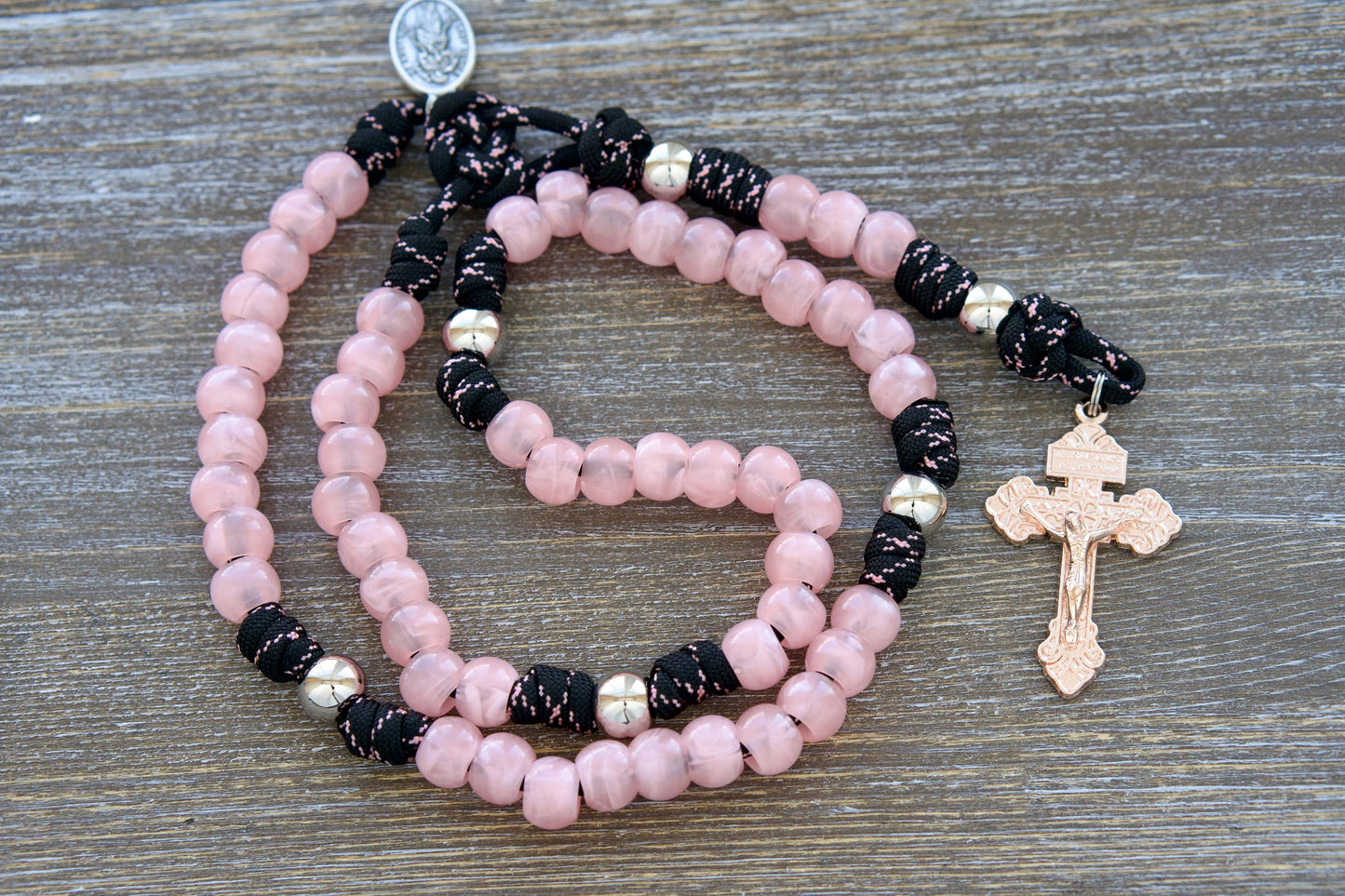 Our Lady Untier of Knots 5 Decade Paracord Rosary featuring pink acrylic Hail Mary beads, silver Our Father beads, black and pink paracord, and a unique rose gold pardon crucifix. Inspired by the devotional medal honoring Our Lady's intercession for resolving life's challenges.