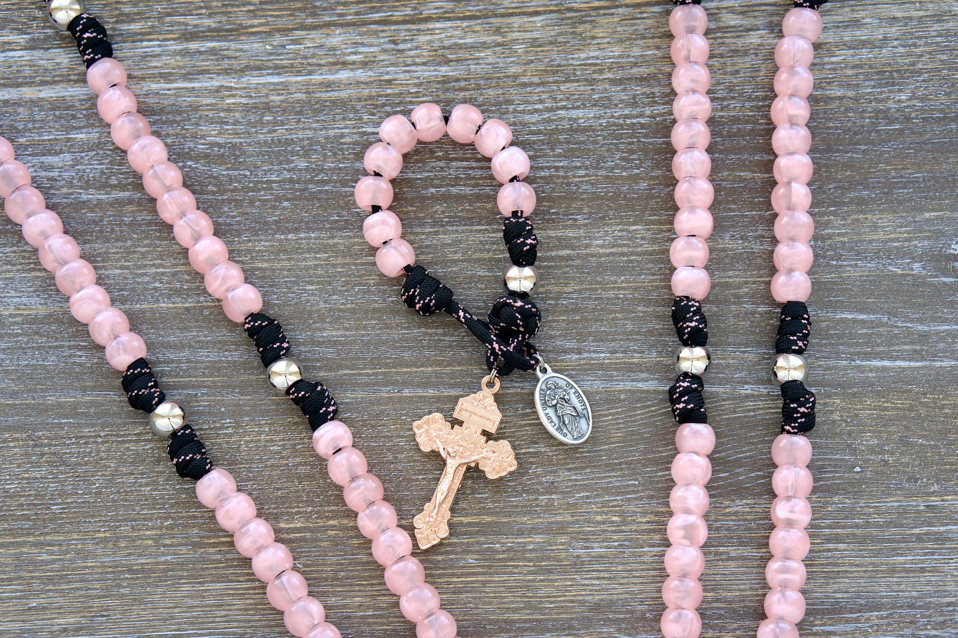 Pocket paracord rosary featuring pink acrylic Hail Mary beads, a silver Our Father bead, black paracord with pink accent, Our Lady Untier of Knots medal, and rose gold pardon crucifix.