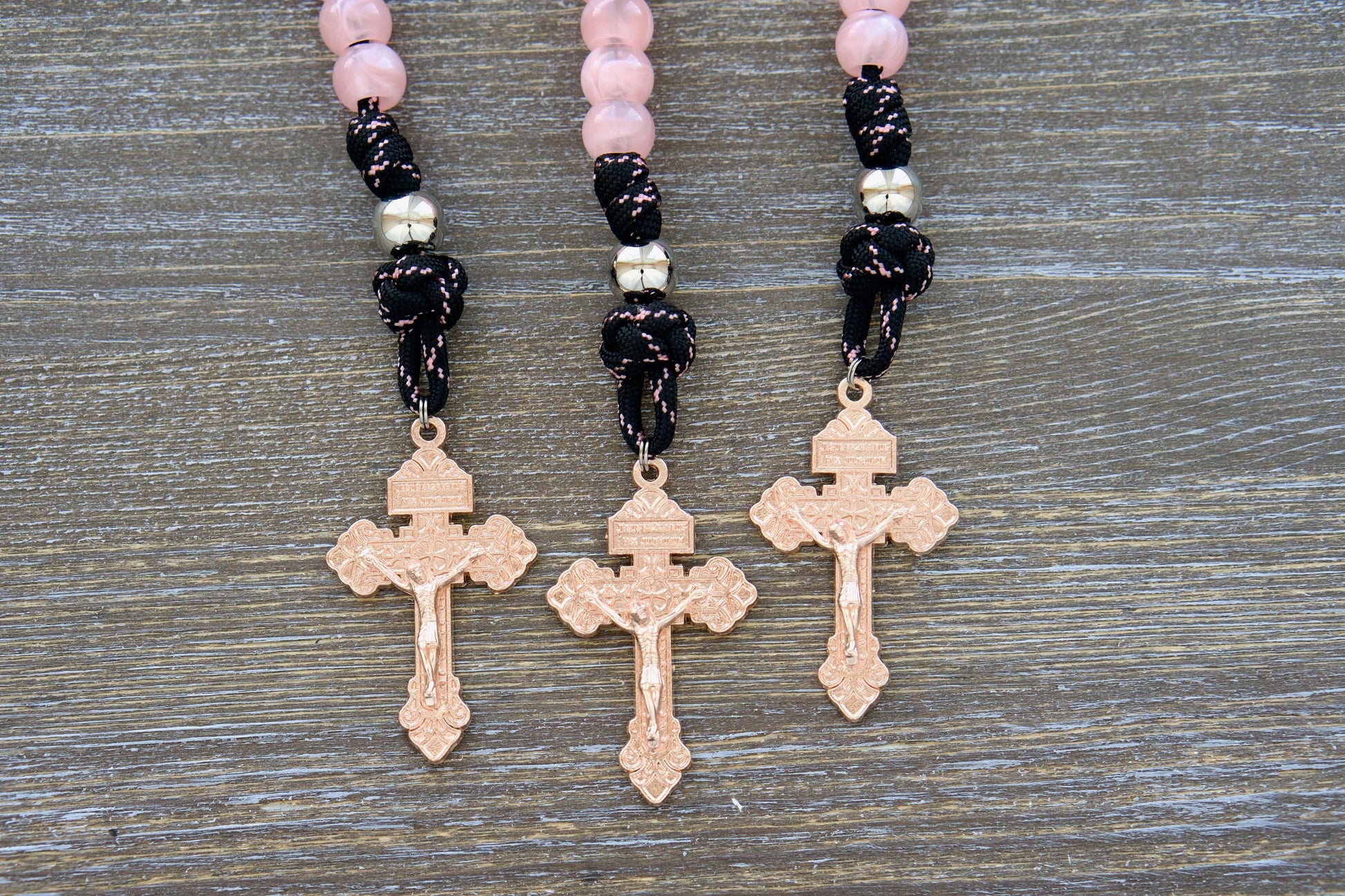 A close-up image of a single decade Our Lady Untier of Knots pocket paracord rosary. It features pink acrylic Hail Mary beads, a shiny silver Our Father bead, black paracord with a pink accent stripe, an Our Lady Untier of Knots devotional medal, and a unique rose gold pardon crucifix.