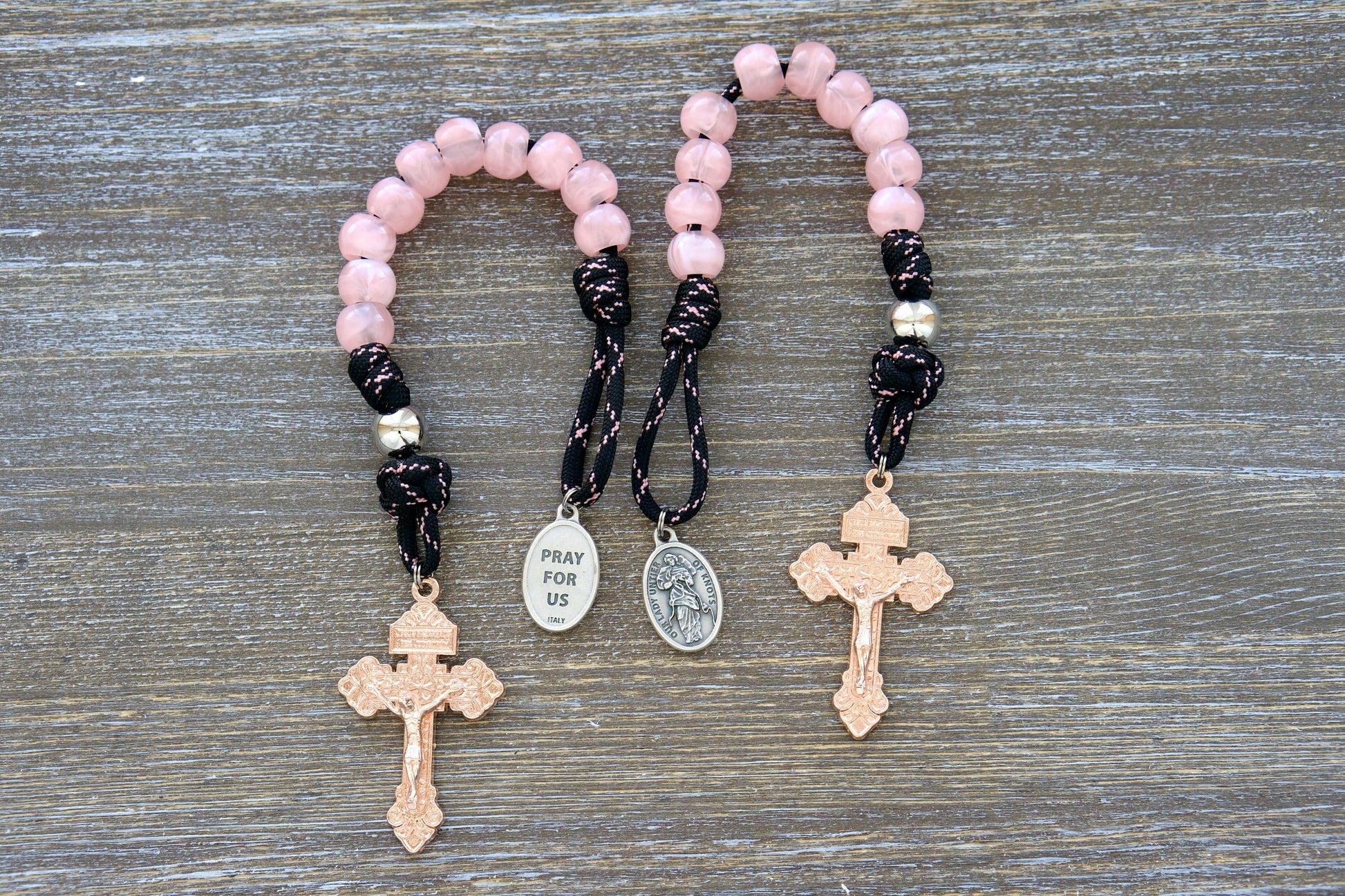 Single decade Our Lady Untier of Knots pocket paracord rosary featuring pink acrylic gemstone Hail Mary beads, a silver Our Father bead, black and pink accented paracord, an Our Lady devotional medal, and a rose gold Pardon crucifix.