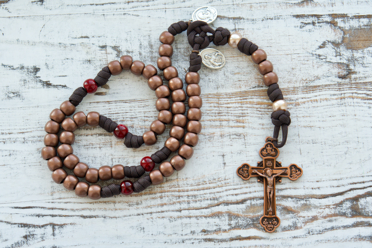 St. Padre Pio's Intercession - 5 Decade Paracord Rosary, featuring a stunning design with brown and red colors, antique copper Hail Mary beads, deep maroon Our Father beads honoring St. Padre Pio's Stigmata, devotional medals for St. Padre Pio and the Sacred Heart of Jesus, and a large, heavy duty copper Crucifix.