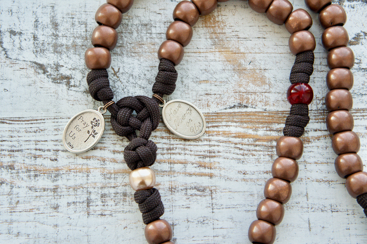 St. Padre Pio's Intercession - 5 Decade Paracord Rosary, featuring maroon red beads honoring his four Stigmata wounds, antique copper Hail Mary beads, two devotional medals (St. Padre Pio and Sacred Heart of Jesus), and a heavy duty copper Crucifix.