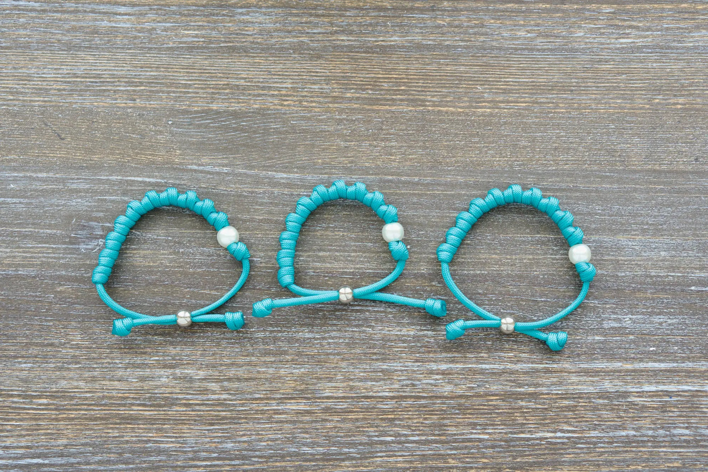 Teal blue paracord 550 knotted rosary bracelet features a white Our Father bead, silver accent, perfect for adults.