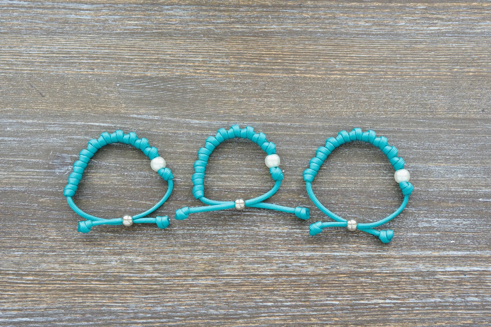 Teal blue paracord 550 knotted rosary bracelet features a white Our Father bead, silver accent, perfect for adults.