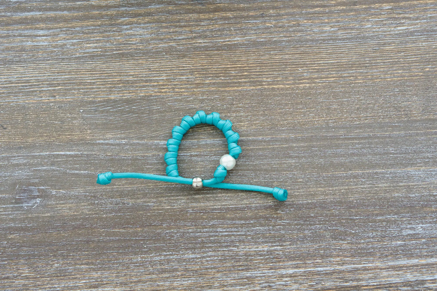 Teal blue paracord knotted rosary bracelet features a 12mm white acrylic Our Father bead and silver knot.