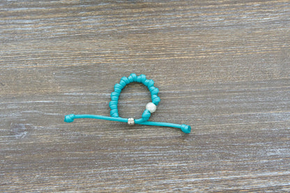 Teal blue paracord knotted rosary bracelet features a 12mm white acrylic Our Father bead and silver knot.