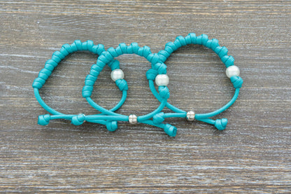 The Peaceful Waters rosary bracelet features teal paracord, a white acrylic Our Father bead, a silver tie bead.