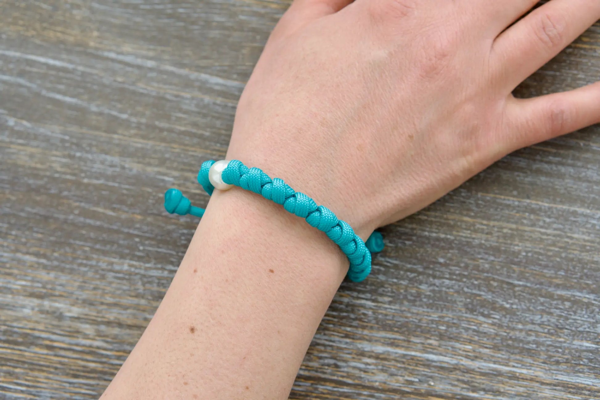 This teal blue paracord 550 Peaceful Waters rosary bracelet features a white 12mm Our Father bead, silver 10mm bead.