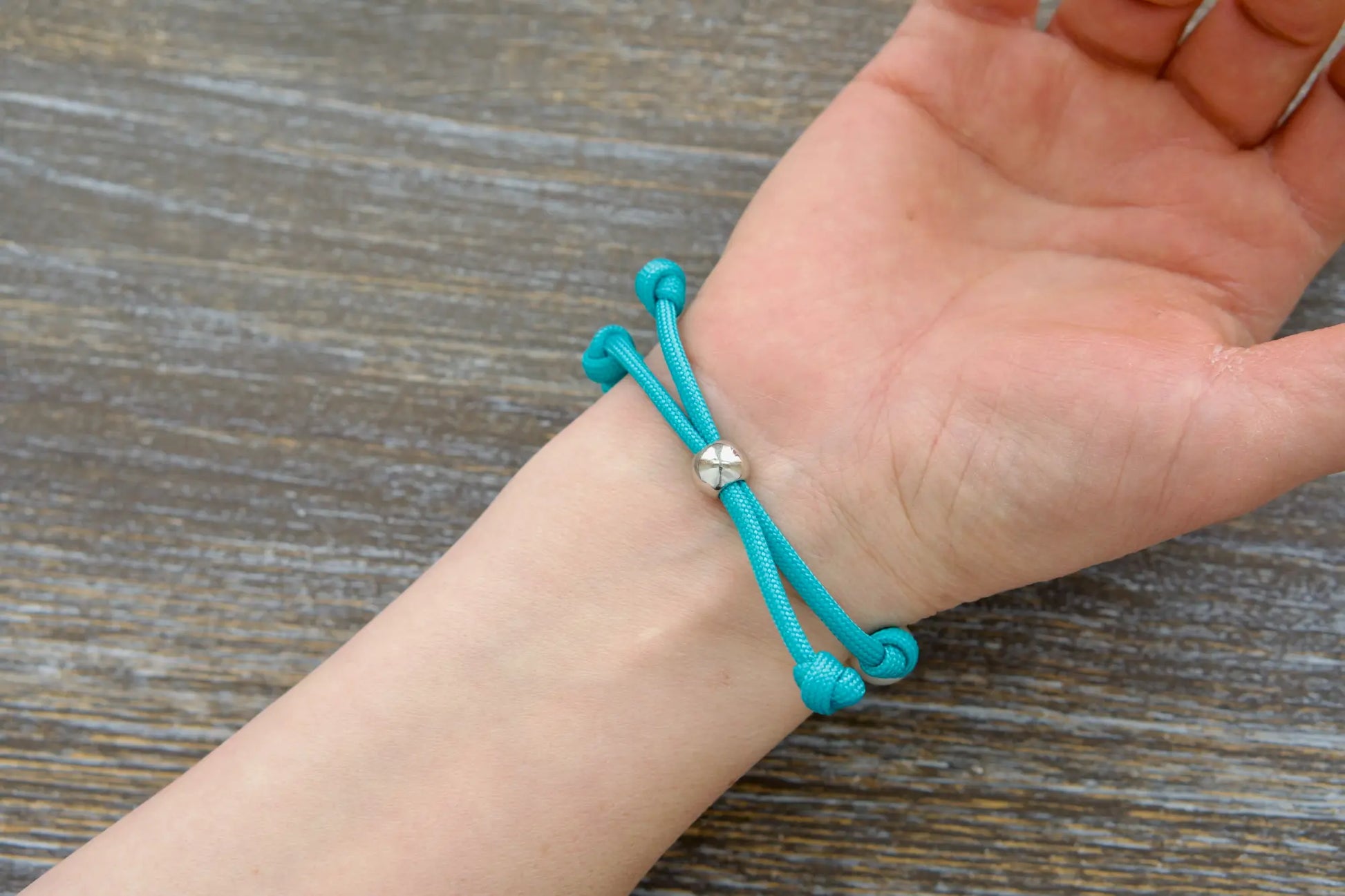 Teal blue paracord rosary bracelet knotted with white Our Father bead, silver accent bead.