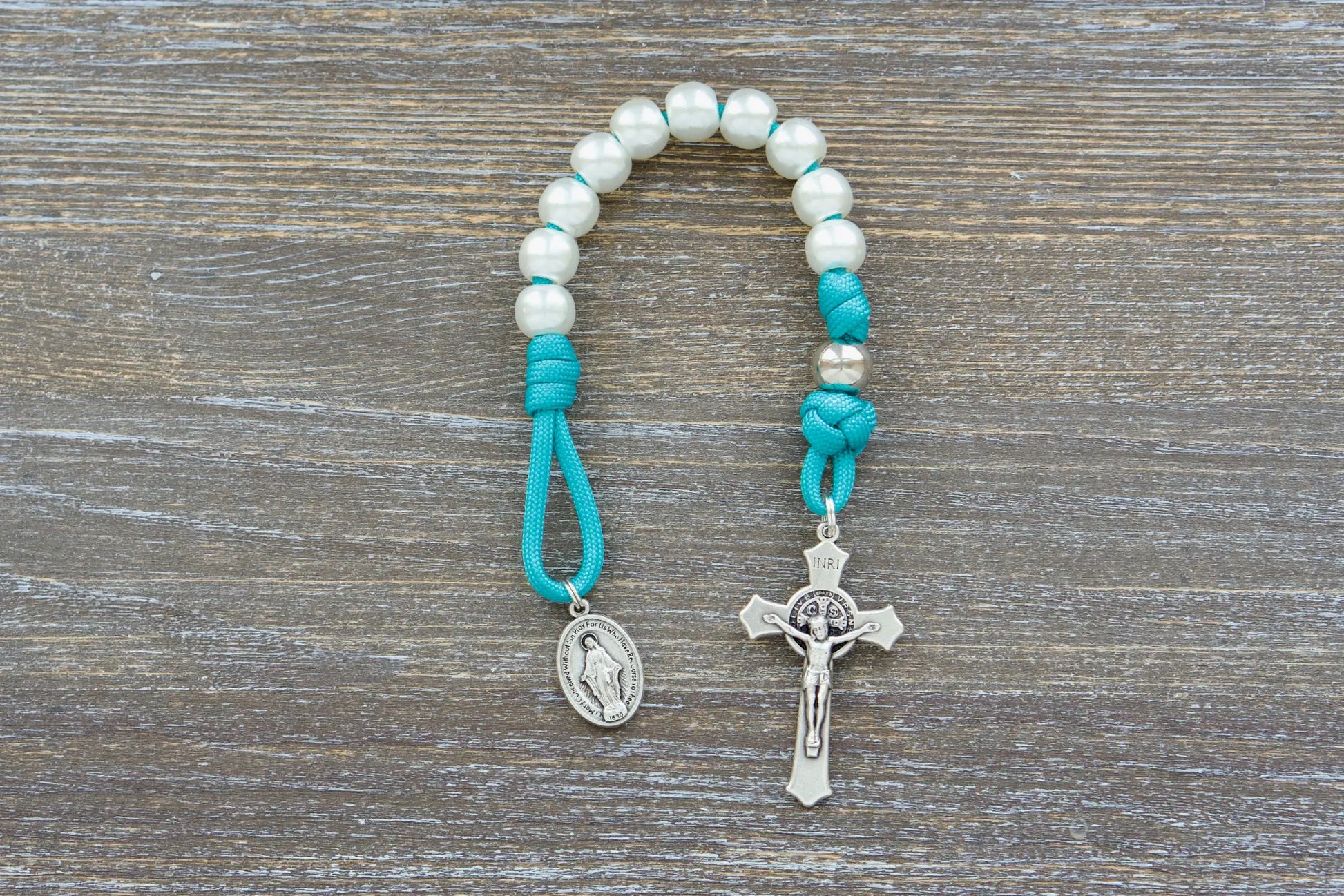 Teal blue Peaceful Waters paracord rosary featuring pearl white beads, silver accents, and a St. Benedict Crucifix.