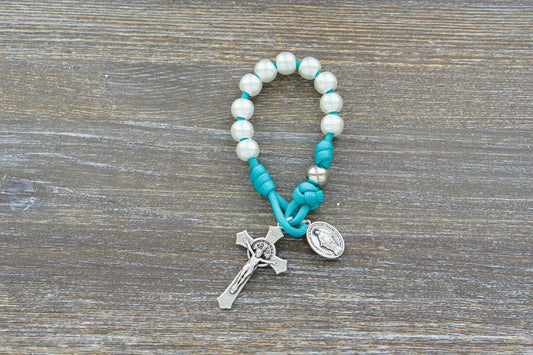 The Peaceful Waters pocket rosary features teal paracord 550, pearl-white and silver beads, a 2-inch St. Benedict Crucifix, and a 1-inch Miraculous Medal.