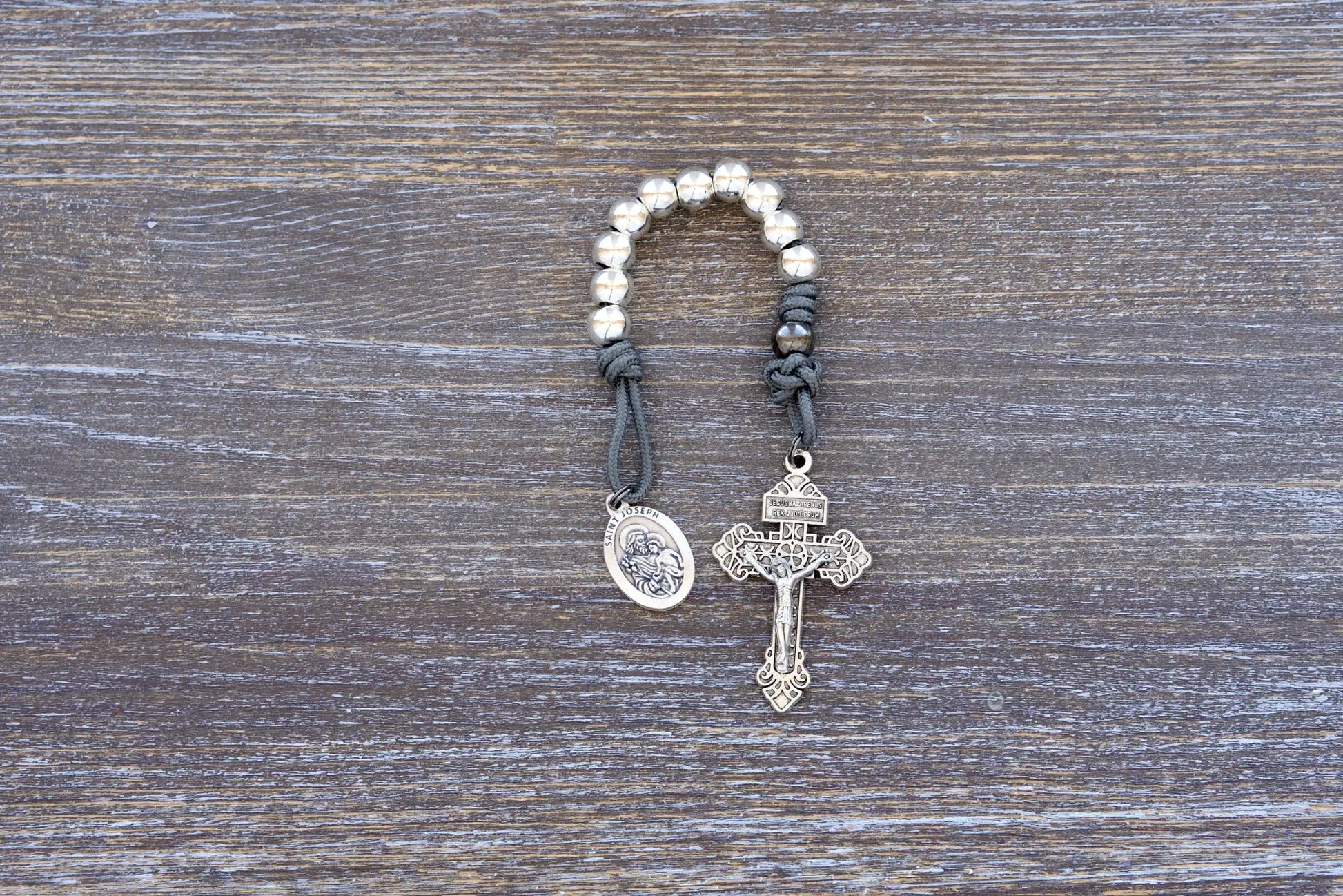 St. Joseph pocket paracord rosary with silver beads, gray cord, and holy medal in soft natural light.