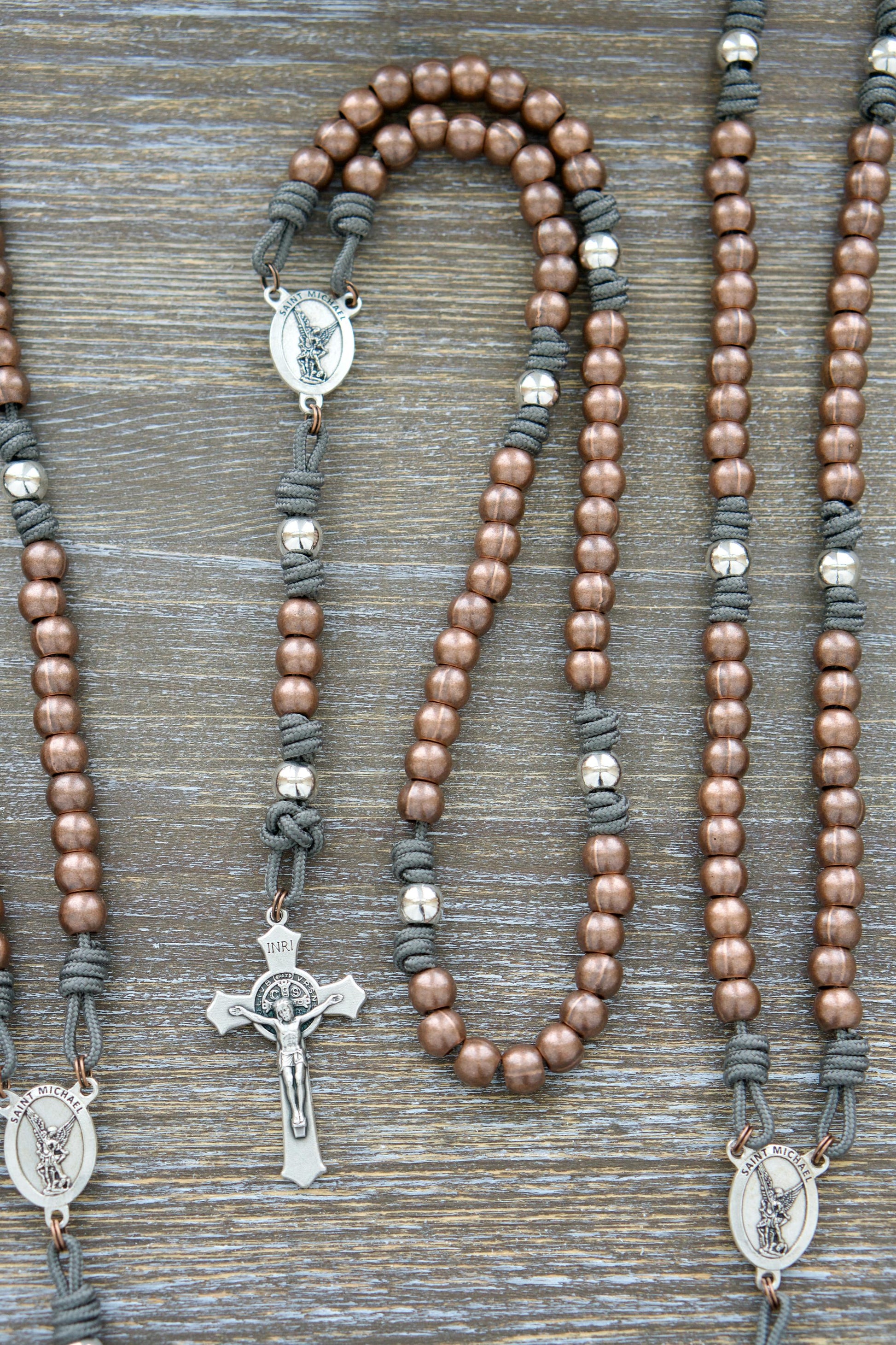 Premium Metal Paracord Rosary, featuring rugged grey paracord, robust copper Hail Mary beads, shimmering silver Our Father beads, and a silver St. Michael centerpiece devotional medal on a 2" St. Benedict crucifix, perfect for spiritual protection and unwavering faith in the Church Militant.