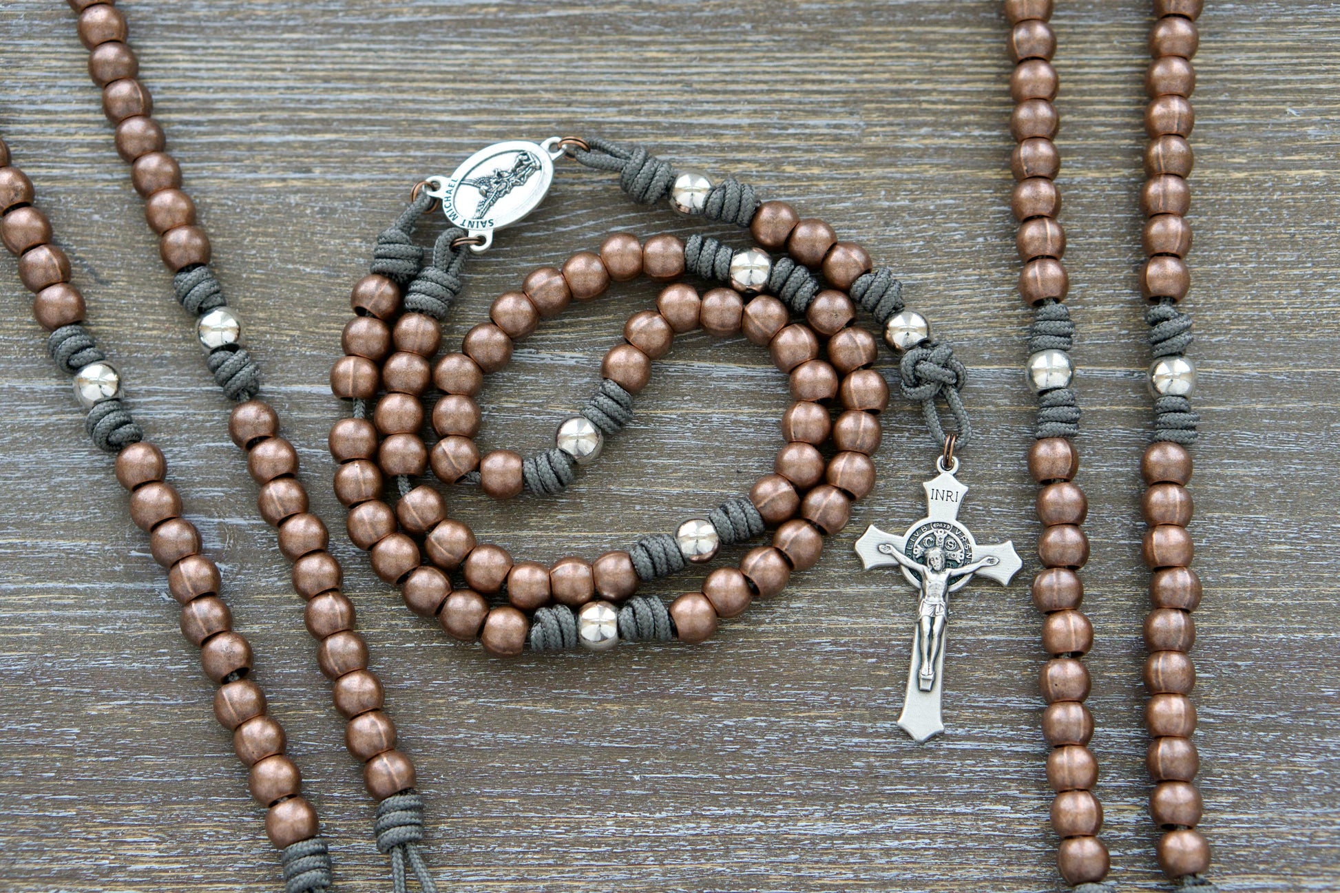 Premium Metal Paracord Rosary, featuring grey paracord, robust copper Hail Mary beads, shimmering silver Our Father beads, silver St. Michael centerpiece, and a 2-inch St. Benedict crucifix, perfect for Catholic spiritual warriors.