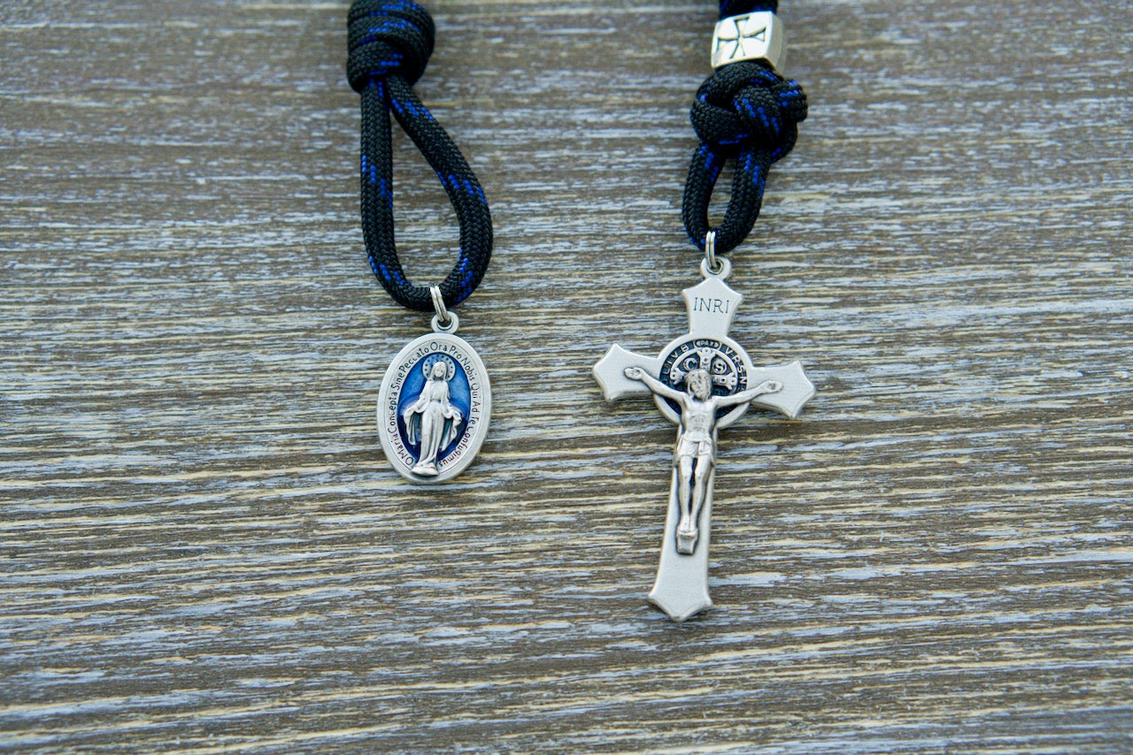 The Solemn Crusader - Blue Black and Silver 1 Decade Paracord Rosary: Embrace your unwavering devotion with this durable, premium, and unbreakable paracord rosary. Crafted for the modern-day crusader, this Catholic gift features black paracord, 12mm shiny black Hail Mary beads, silver metal alloy Our Father beads, a protective silver St. Benedict crucifix, and a blue enamel Miraculous Medal.
